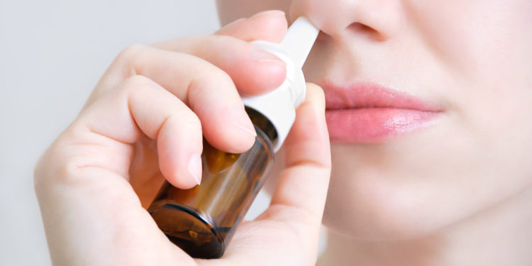 A young woman sprays a nasal spray in her nose