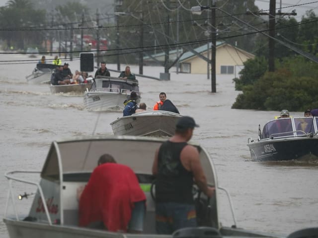 People drive motor boats on a flooded road.