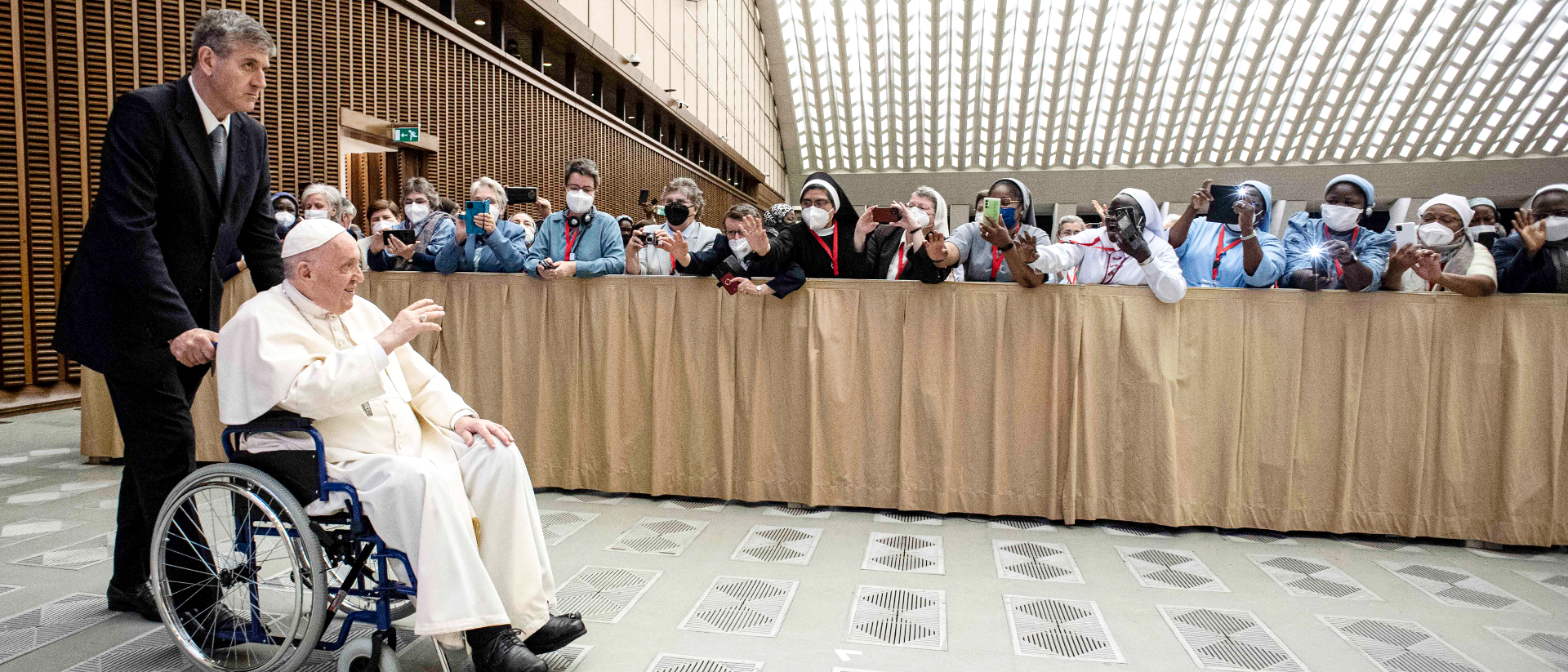 Papst Franziskus sitzt im Rollstuhl und winkt lachend Teilnehmern bei der Generalaudienz am 5. Mai 2022 im Vatikan.
