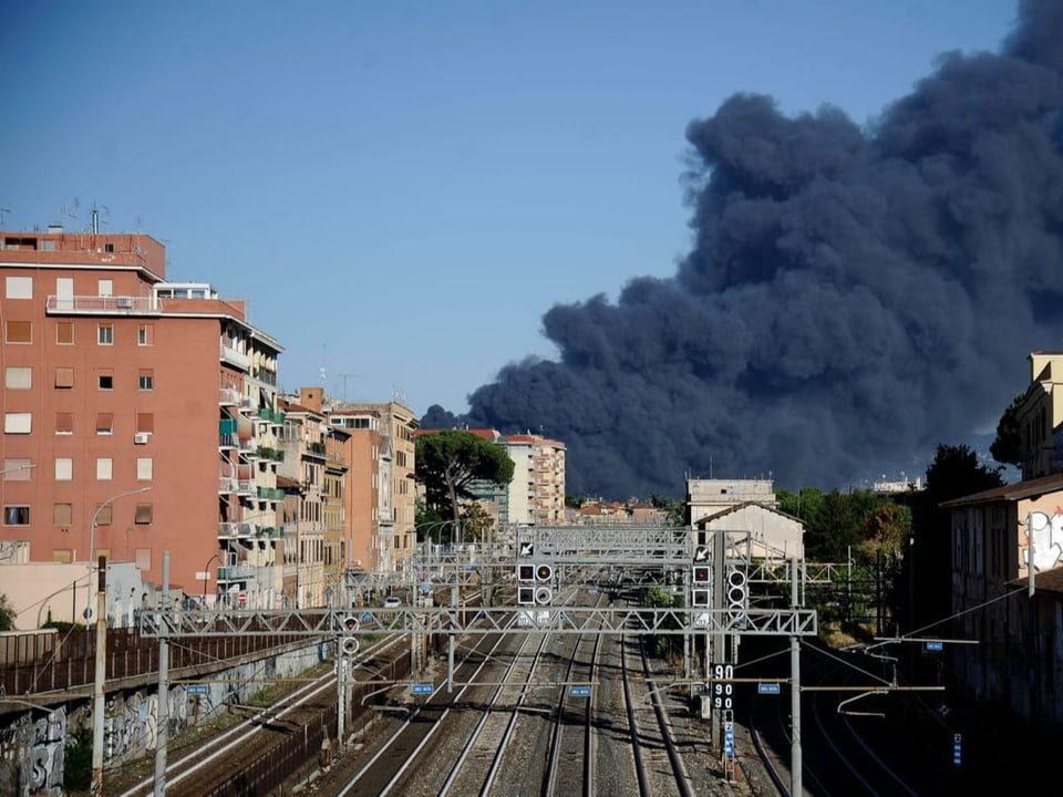 View of a railway track in Rome, with a thick cloud of black smoke in the background