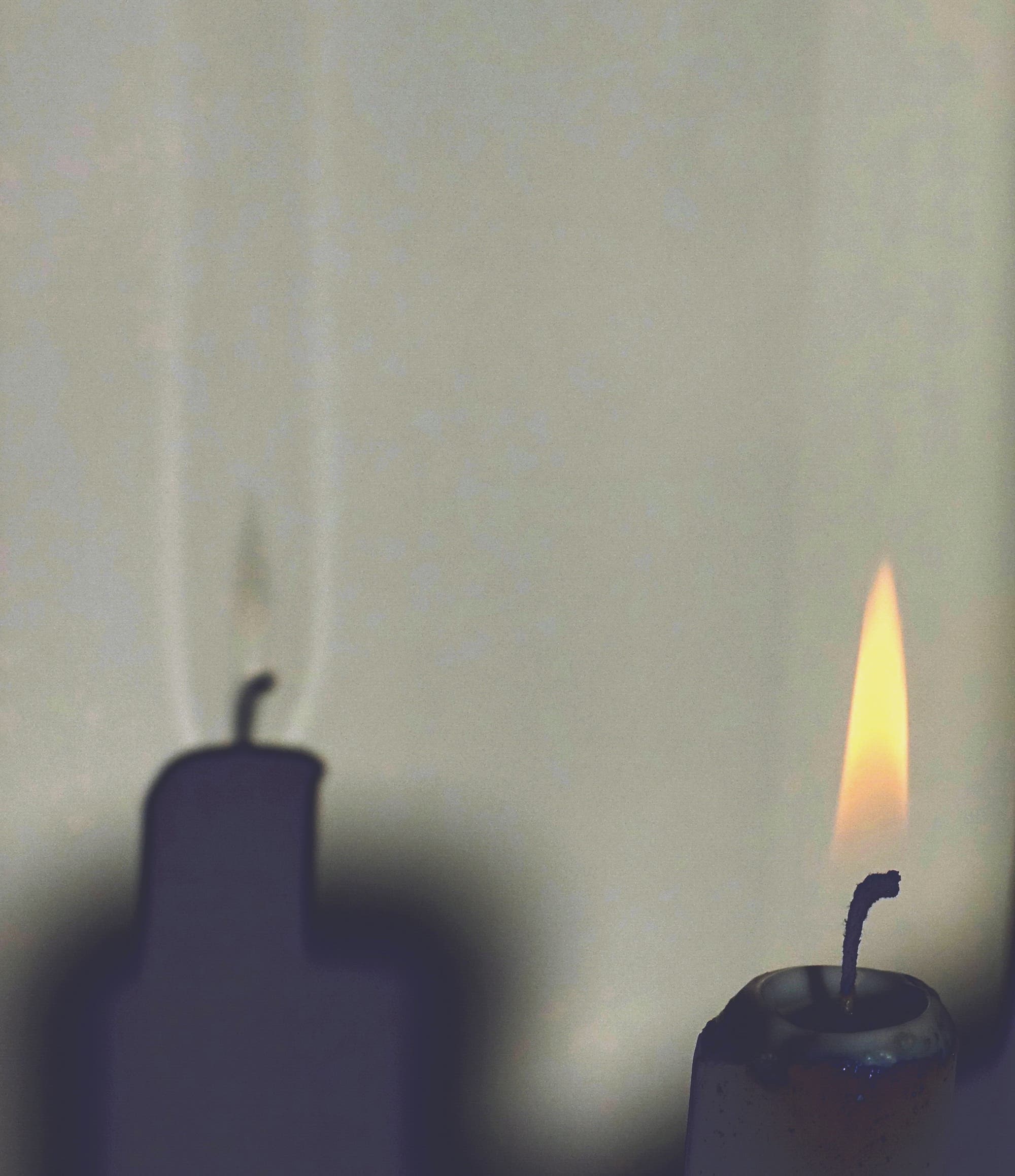 A burning candle standing in the sunlight.  On the white wall it can be seen that the shadow of the flame is surrounded by two vertical bands of light.  Above the wick is a similar bright spot.